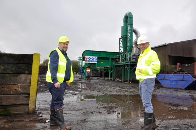 Two people pose for the camera wearing hard hats, high-visibility jackets and boots.